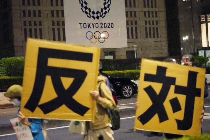 지난  23일 '(올림픽)반대'라고 적힌 피켓을 든 시위대가 일본 도쿄도청 앞을 행진하고 있다. 연합뉴스