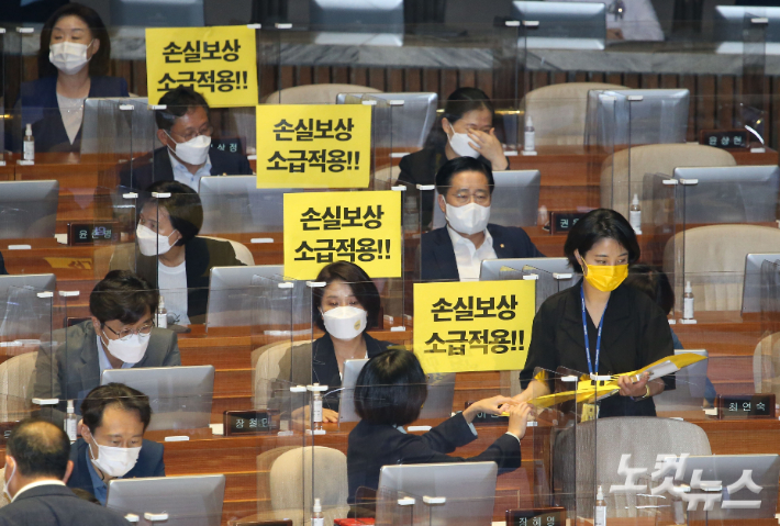 정의당 류호정 의원이 지난 1일 국회 본회의에서 동료의원들에게 '손실보상 소급적용'이라고 기재된 손 피켓을 나눠주고 있다. 윤창원 기자