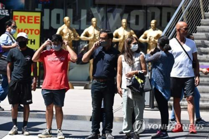 19일(현지시간) 실내 마스크 착용 의무화가 복원된 미 캘리포니아주 LA의 할리우드에서 길을 건너려 신호를 기다리는 사람들이 마스크를 쓴 채 서 있다. 연합뉴스