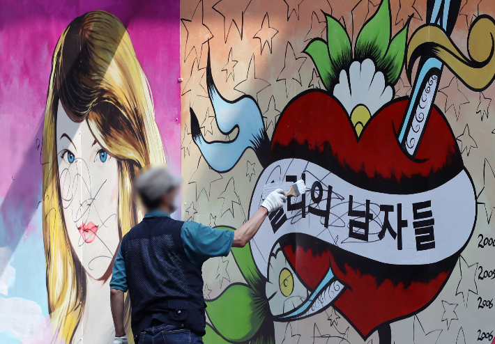 30일 오전 한 건물 관계자가 벽화의 글자를 흰색 페인트로 칠하고 있다. 연합뉴스