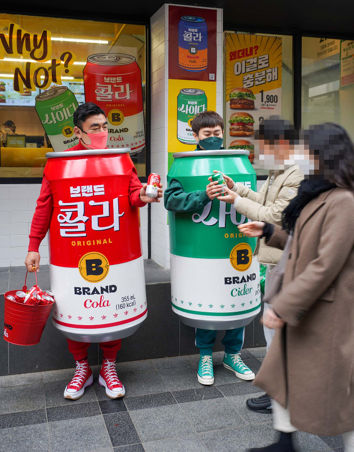 14일 서울 중구 무교동 노브랜드 버거 서울시청점 앞에서 신세계푸드 송현석 대표이사와 이대희 수원호매실점 브랜드 파트너(가맹점주)가 이날 론칭한 '브랜드 콜라'와 '브랜드 사이다'를 알리기 위해 특별 제작한 콜라맨, 사이다맨 의상을 착용하고 직접 제품을 나눠주며 홍보에 나섰다. 신세계푸드 제공 