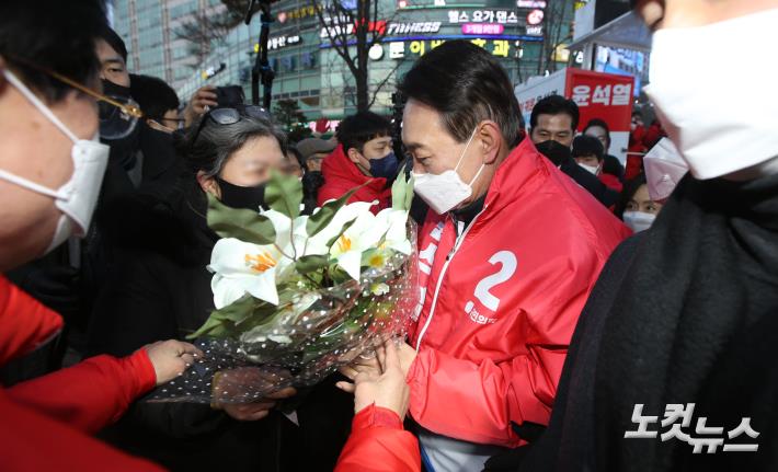 국민의힘 윤석열 대선 후보가 17일 오후 서울 종로구 동묘앞역 인근에서 유세를 마친 뒤 차량으로 향하는 도중 한 시민에게 꽃다발을 전달받고 있다.