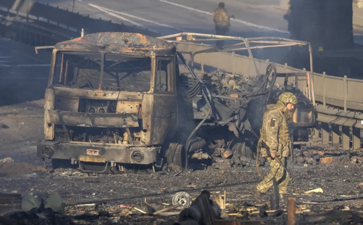26일(현지시간) 우크라이나 키예프 거리에서 불탄 군용 트럭 잔해 앞으로 우크라이나군인이 지나고 있다. 연합뉴스