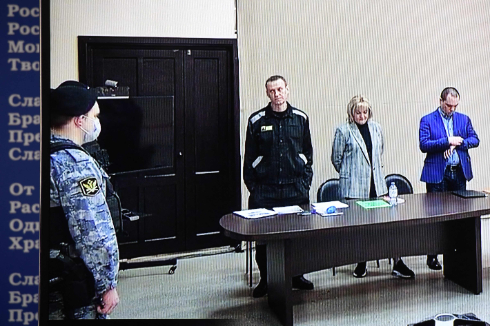 러시아 야권 지도자 알렉세이 나발니(중앙)가 22일(현지시간) 블라디미르주 파크로프의 제2 교도소(IK-2) 내부 법정에서 열린 재판에서 변호사와 함께 기립한 모습이 모니터 화면에 비치고 있다. 연합뉴스