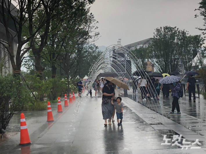 6일 재개장한 서울 광화문광장을 찾은 모자(母子)가 빗속에 우산을 쓰고 '터널 분수'를 통과하고 있다. 이은지 기자 