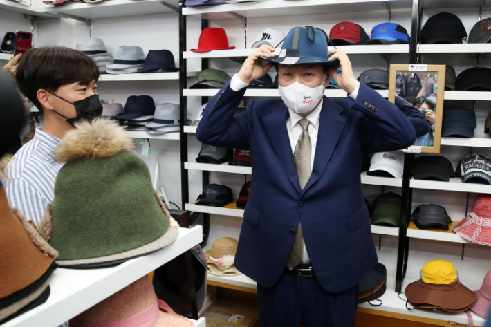 윤석열 대통령이 26일 오후 대구 중구 서문시장 내 모자 가게를 방문, 모자를 써보며 상인들과 대화하고 있다. 연합뉴스