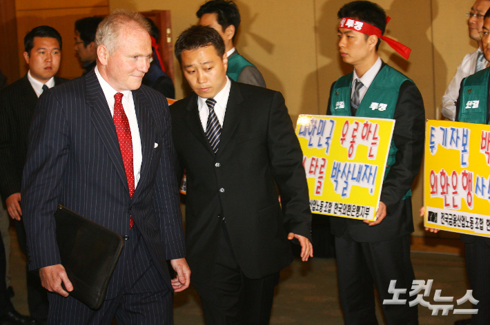 지난 2006년 4월 18일 론스타의 존 그레이켄 회장이 서울 63빌딩 체리홀에서 열린 기자회견을 참석을 위해 회견장으로 들어서던 중 입구에서 시위 중인 외환은행 노조원들을 바라보고 있다. 