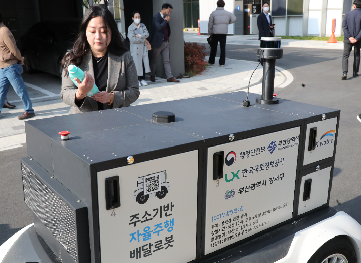 지난해 11월 부산 강서구 에코델타시티 스마트빌리지에서 열린 '주소기반 자율주행 로봇 배송' 시연회에서 이용자가 로봇이 배송한 물건을 전달받고 있다. 이 기술은 이용자가 로봇 배송으로 주문하면, 편의점 점주가 주문 내용을 확인해 로봇에 물건을 싣고 배송하도록 하는 방식이다. 연합뉴스