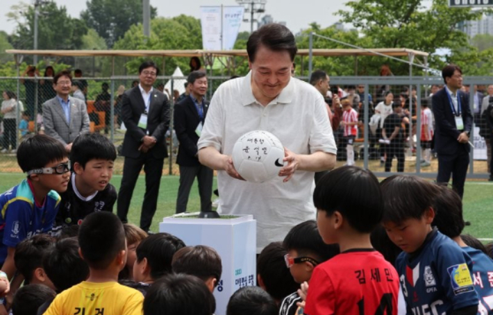 윤석열 대통령이 휴일인 14일 서울 용산 어린이정원 내 축구장에서 대통령실 초청 전국 유소년 축구대회에 참가한 어린이 선수들이 지켜보는 가운데 축구공에 사인하고 있다. 연합뉴스