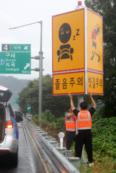 한국도로공사 순천지사 직원들이 호남고속도로 천안방면 주의표지판 방향을 졸음주의에서 빗길주의로 돌리고 있다. 연합뉴스