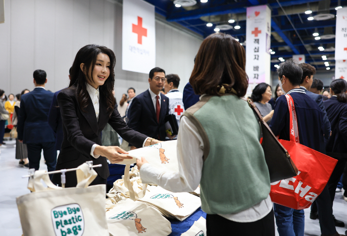 김건희 여사가 31일 서울 강남구 코엑스에서 열린 2023 적십자 바자 행사에서 플라스틱 소비 중단을 의미하는 '바이바이 플라스틱(Bye Bye Plastic)' 에코백을 방문자들에게 전달하고 있다. 대통령실 제공