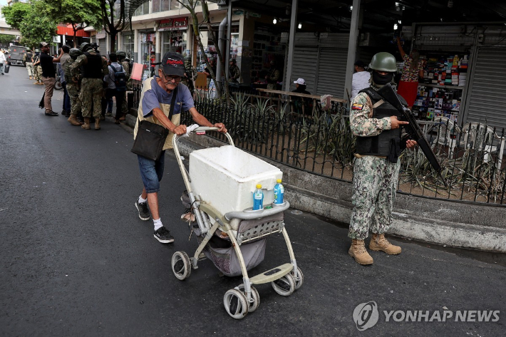 (키토 로이터=연합뉴스) 11일(현지시간) 에콰도르 수도 키토에서 한 시민이 무장한 군 장병 옆을 지나가고 있다. 2024.1.12 연합뉴스