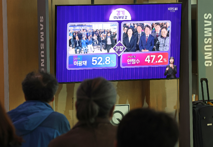 제22대 국회의원선거일인 10일 오후 서울 중구 서울역에서 시민들이 더불어민주당 이광재 후보와 국민의힘 안철수 후보가 출마한 경기 성남분당 갑 출구조사 관련 방송을 지켜보고 있다. 연합뉴스 