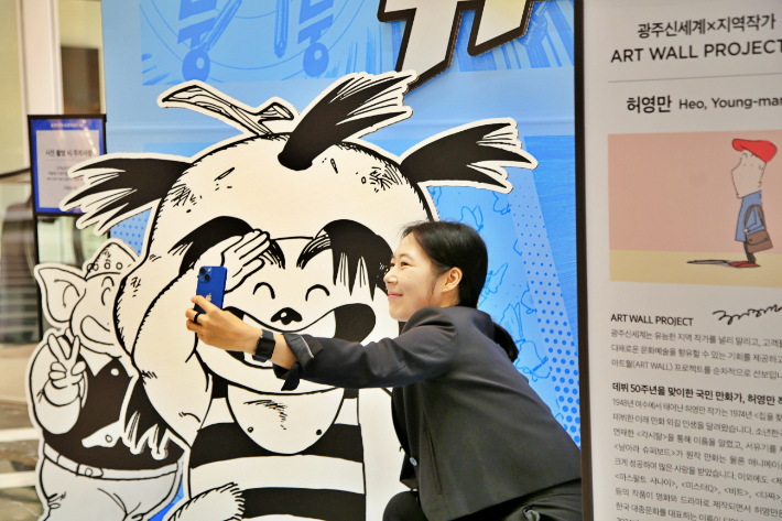 광주신세계 1층에 마련된 허영만 화백의 대표작 '날아라 슈퍼보드' 아트월 앞에서 인증샷을 찍고 있다. 광주신세계 제공