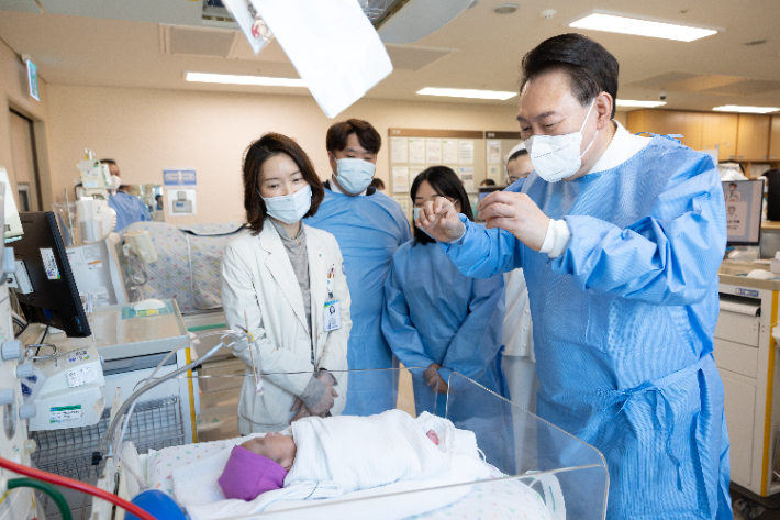 윤석열 대통령이 28일 서울성모병원에서 '이른둥이 지원 간담회' 전 입원 중인 다섯쌍둥이의 다섯째를 보고 있다. 왼쪽부터 주치의 윤영아 교수, 부모, 윤 대통령. 연합뉴스