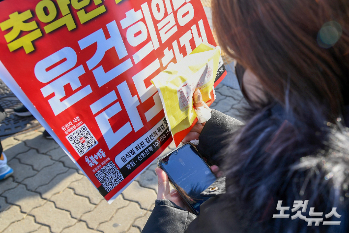 7일 서울 여의도 국회 앞에서 윤석열 정권 퇴진 집회를 하던 시민들이 윤 대통령의 대국민 담화를 시청하고 있다. 박종민 기자