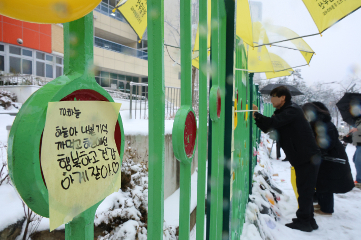 대전 초등학생 김하늘 양 피살사건이 발생한 대전 서구의 한 초등학교 정문에서 12일 오전 학교 관계자가 추모객들이 놓고 간 꽃과 편지 위에 우산을 씌워주고 있다. 연합뉴스