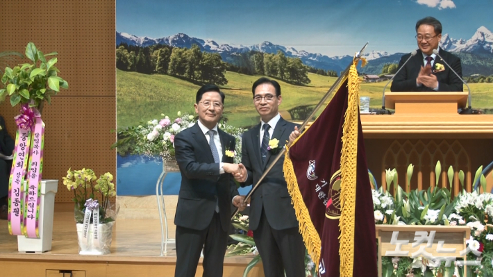 7대 최규완 목사(오른쪽)에게 교회기를 전달하고 있는 6대 최선길 목사(왼쪽). 최진성 아나운서