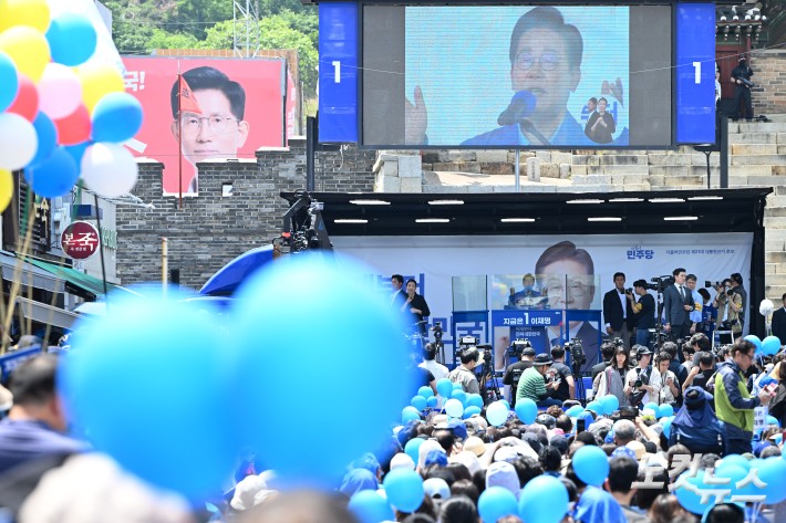이재명 더불어민주당 대선 후보가 26일 경기 수원시 팔달문 영동시장 입구에서 집중유세를 하고 있는 가운데 뒤로 김문수 국민의힘 대선 후보의 현수막이 보이고 있다.