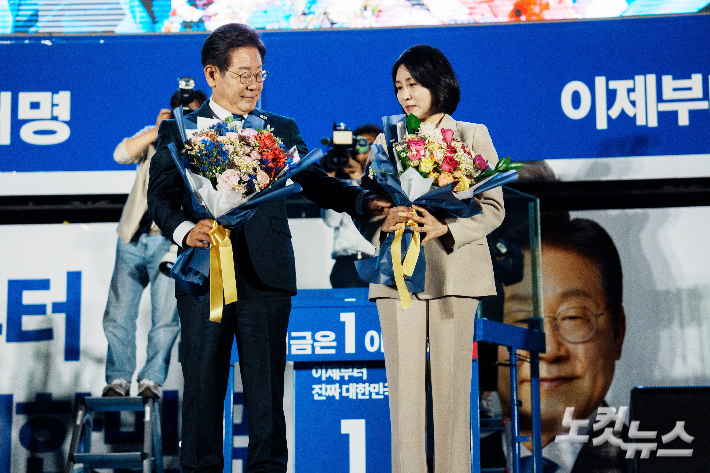 제21대 대통령 당선이 확실시되는 더불어민주당 이재명 대선 후보와 김혜경 여사가 4일 서울 여의도 국회 앞에 마련된 더불어민주당 국민 개표방송 행사에서 꽃다발을 받은 뒤 손을 잡고 있다. 류영주 기자
