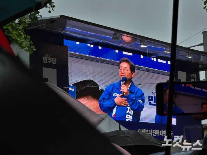 이재명 대통령이 선거운동 기간인 지난달 15일 순천에서 장대비속에 유세하는 것을 우산을 든 시민들이 지켜보거나 촬영하고 있다. 고영호 기자