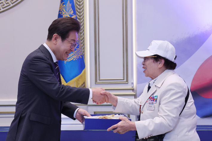 이재명 대통령이 27일 청와대 영빈관에서 열린 '호국 보훈의 달, 대통령의 초대' 행사에서 6·25전쟁에 참전해 유격대원으로 활약했던 여성 참전유공자 이춘자 참전용사에게 광목이불을 선물하고 있다. 연합뉴스 