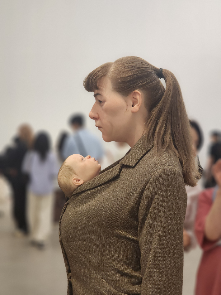 코트 안에 아이를 넣고 두 손에 주황색 비닐봉지를 들고 서 있는 '쇼핑하는 여인'(2013년작). 곽인숙 기자
