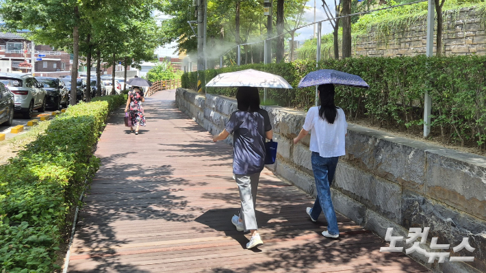 대구 동구의 한 거리에서 시민들이 더위를 피해 양산을 쓴 채 쿨링 포그 밑을 걷고 있다. 정진원 기자