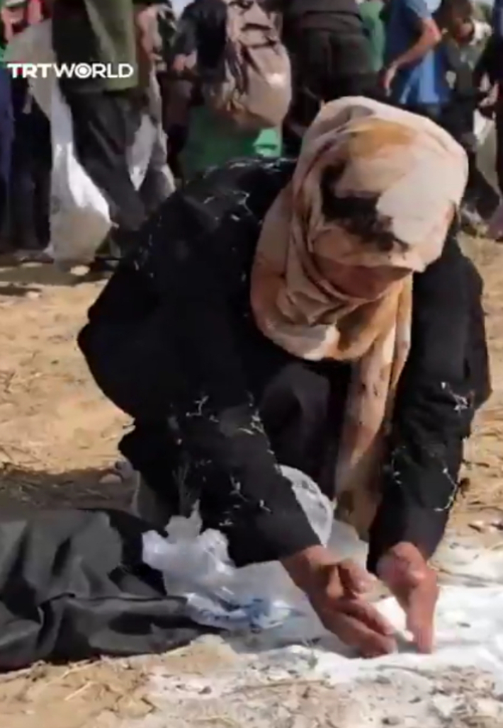 구호물자가 공중에서 투하돼 밀가루가 터져 흙과 섞였지만 한 여성이 손으로 주워 담고 있다. X 캡처