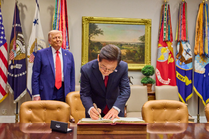 이재명 대통령이 25일(현지시간) 미국 워싱턴 DC 백악관에서 도널드 트럼프 미국 대통령이 지켜보는 가운데 방명록을 작성하고 있다. 연합뉴스