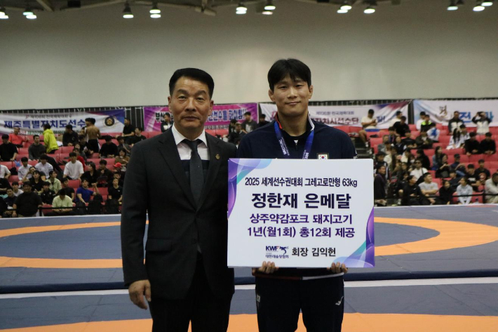 세계선수권대회에서 은메달을 딴 레슬링 국가대표 정한재(오른쪽)가 21일 부산 BEXCO제2전시장에서 대한레슬링협회 김익헌 회장으로부터 1년 치 돼지고기 세트를 포상으로 받은 뒤 웃고 있다. 대한레슬링협회 제공