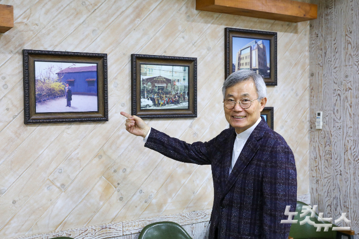 부임 당시 무덤 옆 양철지붕 교회 사진과 서신동 성전 건축 당시 모습을 배경으로, 과거와 현재를 비교하며 이야기를 전하는 홍동필 목사. 최화랑 기자