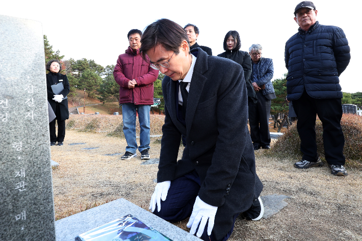  12·3 비상계엄 사태 1주년인 3일 오후 광주 북구 국립 5·18 민주묘지에서 국민의힘 조경태 의원(부산 사하구을)이 무릎을 꿇은 채 문재학 열사의 묘소를 참배하고 있다.  사진 연합뉴스 제공