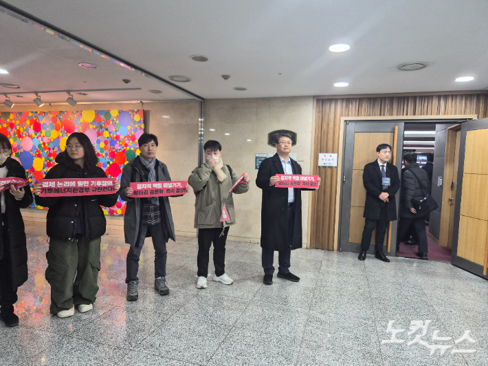 기후에너지환경부가 7일 국회의원회관 제2소회의실에서 '바람직한 에너지믹스 2차 정책토론회'를 개최한 가운데, 행사장 입구에서 시민활동가들이 피켓을 들고 침묵시위를 시작하는 모습. 우측으로 보이는 문이 행사장으로 들어가는 유일한 입구로, 2명의 직원이 사전 등록 여부를 확인해 입장을 제한했다. 최서윤 기자 