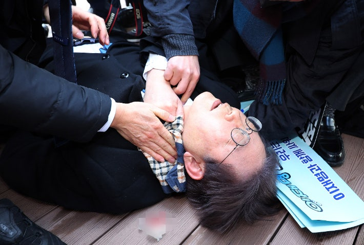지난 2024년 1월 당시 더불어민주당 이재명 대표가 부산 강서구 가덕신공항 부지를 둘러본 뒤 왼쪽 목 부위 피습을 당해 바닥에 누워 병원 호송을 기다리고 있다. 연합뉴스