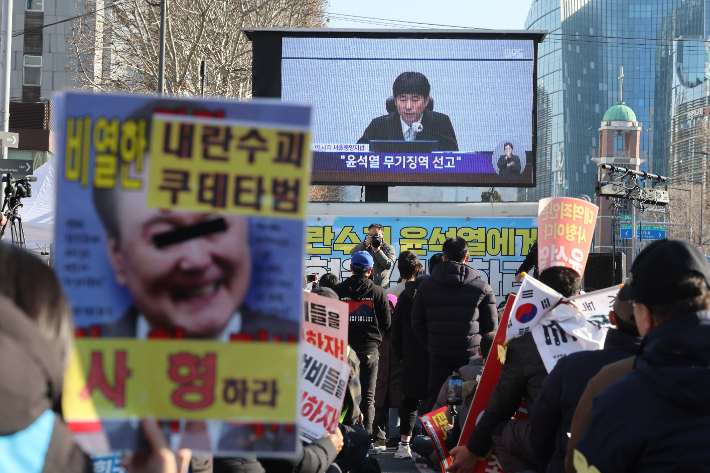 촛불행동 관계자들이 19일 서울중앙지법 인근에서 12·3 비상계엄과 관련해 내란 우두머리 혐의로 기소된 윤석열 전 대통령에 대한 1심 선고 생중계를 시청하고 있다. 이날 재판부는 윤 전 대통령에게 무기징역을 선고했다. 연합뉴스
