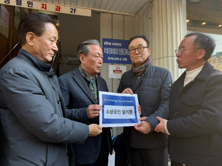 송치영(오른쪽에서 두 번째) 소상공인연합회장이 10일 민주당 김동아 의원 지역위원회 사무실 앞에서 류한수(왼쪽에서 두 번째) 김동아 의원 지역특보에게 대형마트 새벽배송 허용 법안 철회를 촉구하는 소상공인 결의문을 전달하고 있다. 소공연 제공