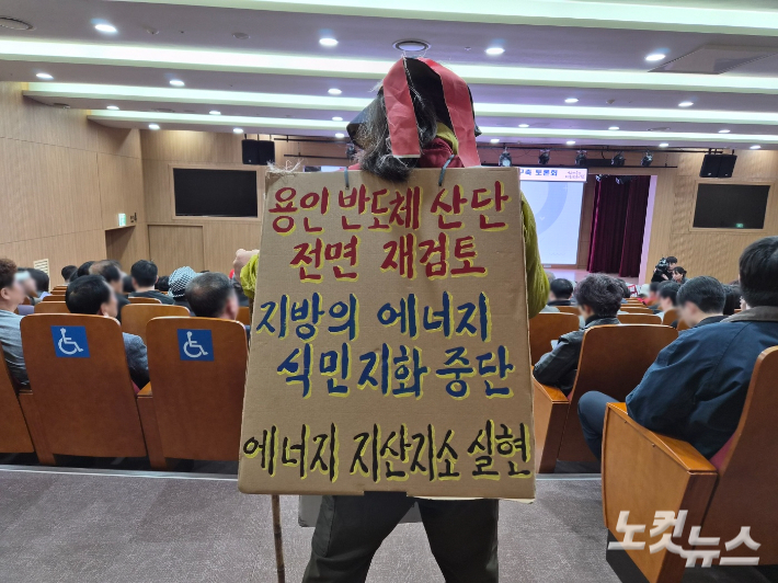 최근 충남에서 열린 국가 균형발전을 위한 전력망 구축 토론회장에서 한 참석자가 '용인 반도체 산단 전면 재검토, 지방의 에너지 식민지화 중단, 에너지 지산지소 실현'이라고 적힌 팻말을 메고 있다. 김정남 기자
