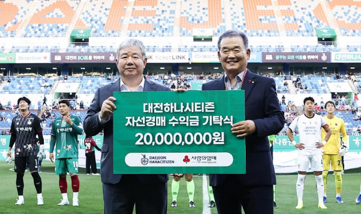 대전하나시티즌 정태희 이사장(사진 왼쪽)이 대전월드컵경기장에서 대전사회복지공동모금회 유재욱 회장에게 자선경매 수익금 2천만 원을 전달하고 있다. 대전하나시티즌 제공