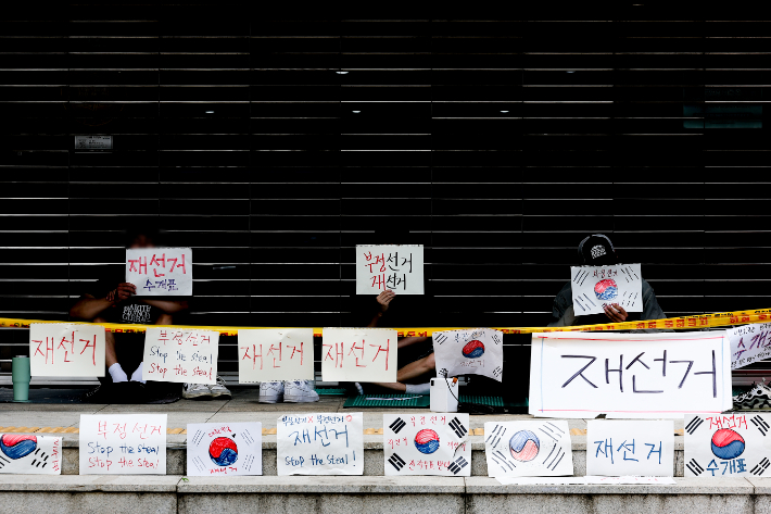 6·3 지방선거 투표용지 부족 사태를 규탄하며 재선거를 요구하는 '잠실 개표소 봉쇄 시위'가 계속되고 있는 9일 서울 송파구 올림픽공원 핸드볼경기장 출입구 앞에서 참가자들이 손팻말을 들고 있다. 연합뉴스