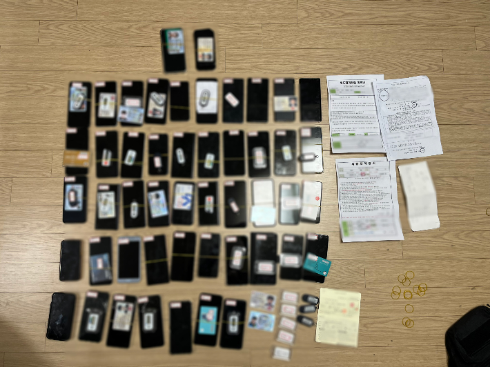 경찰이 자금세탁 조직 총책의 주거지에서 압수한 타인 명의 휴대전화와 신분증, OTP, 통장 등 증거물. 광주경찰청 제공