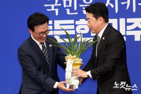 더불어민주당 김민석 신임 당대표가 18일 서울 여의도 국회에서 강훈식 대통령 비서실장으로부터 이재명 대통령의 축하난을 전달받고 있다.