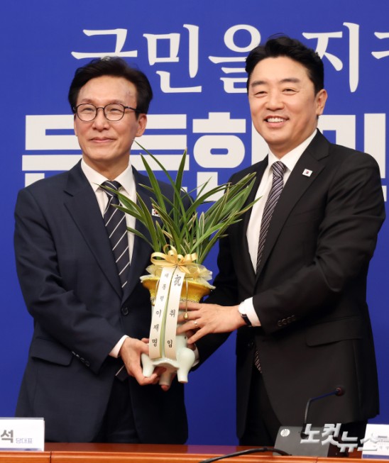 더불어민주당 김민석 신임 당대표가 18일 서울 여의도 국회에서 강훈식 대통령 비서실장으로부터 이재명 대통령의 축하난을 전달받고 있다.