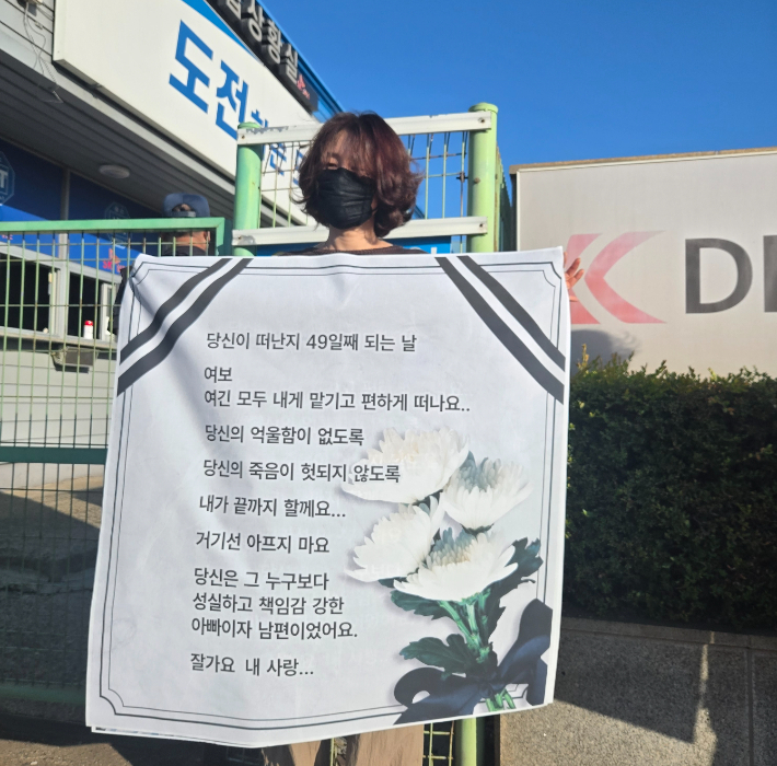 10일 오전 고 김승준 노동자의 아내가 전남광주통합특별시 영암군 대불산단의 대한조선 공장 앞에서 고인을 그리워하는 글을 들고 서 있다. 광주전남노동안전보건지킴이 제공