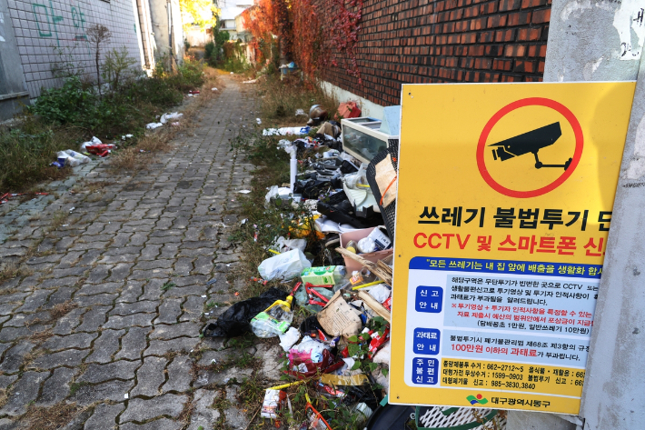 쓰레기 불법투기 신고 안내판 아래 쓰레기가 쌓여있다. 연합뉴스