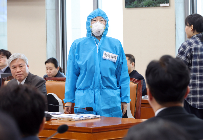 진보당 정혜경 의원이 13일 국회에서 열린 기후에너지환경노동위원회의 고용노동부에 대한 국정감사에서 반도체 협력업체 비정규직 노동자들이 착용하는 방진복을 입고 김영훈 고용노동부 장관에게 설명하고 있다. 연합뉴스